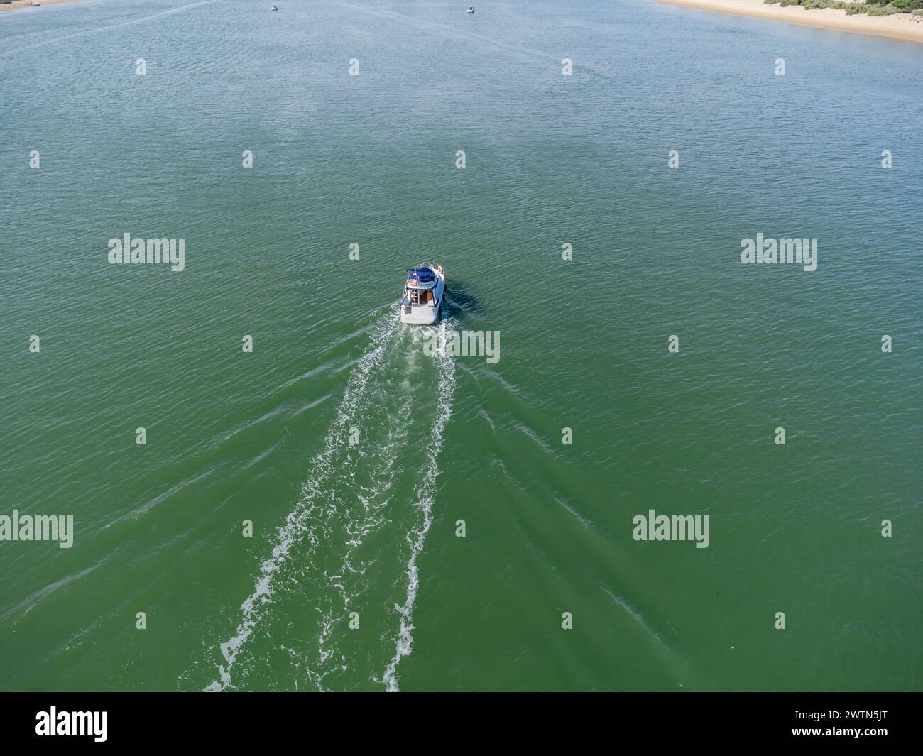 Vista aerea con droni di una barca a motore che naviga nel fiume Piedras tra il villaggio sulla spiaggia di El Portil e la riva di sabbia di la Flecha Foto Stock