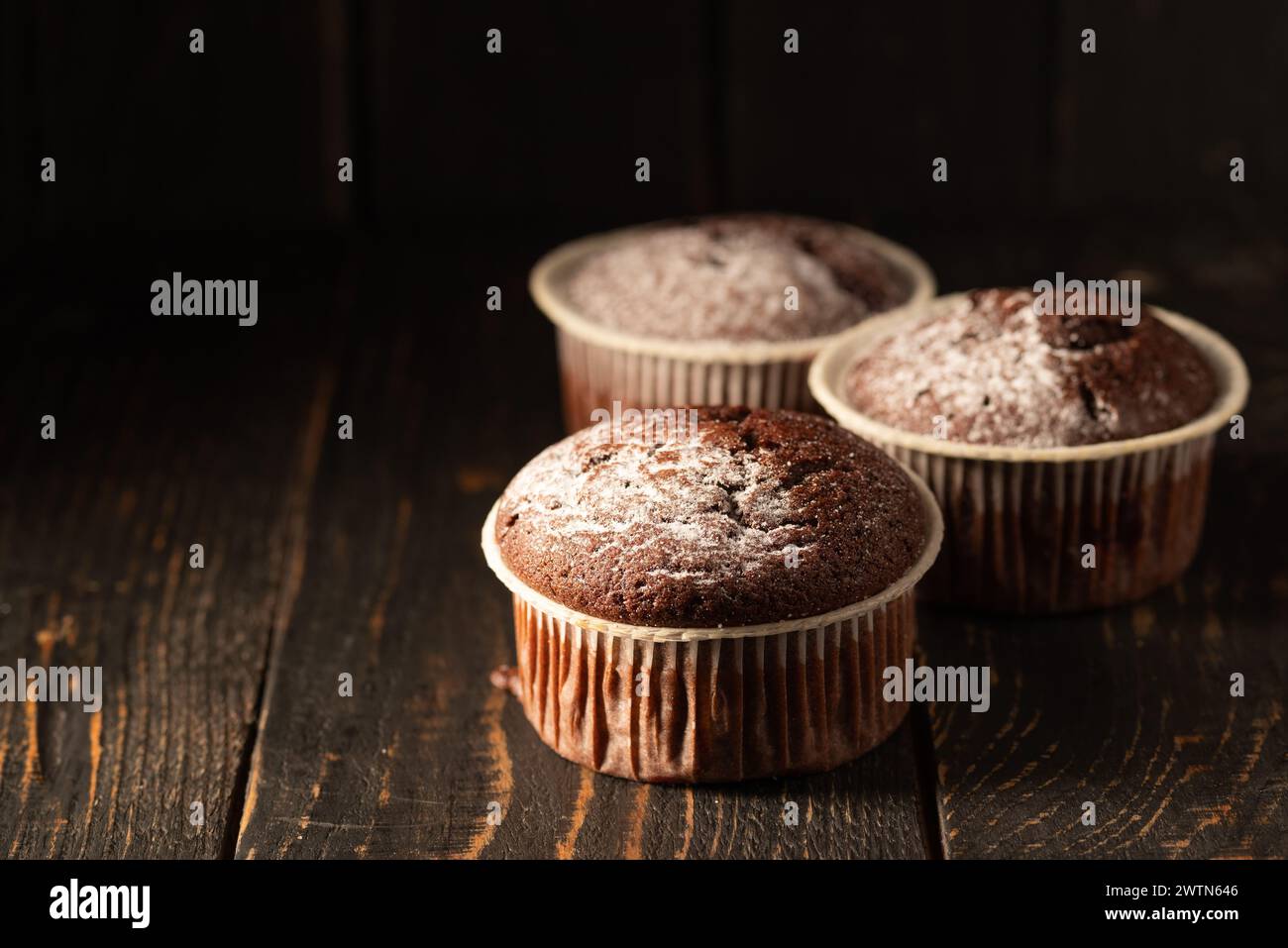 Muffin al cioccolato con zucchero a velo su sfondo nero. Ancora vita da vicino. Oscuro e moody. Foto del cibo Foto Stock