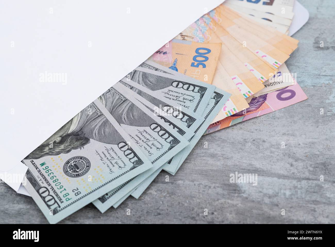 Hryvnias ucraine e dollari americani in una busta bianca su uno sfondo di pietra da vicino. Concetto di pagamento o corruzione. Foto Stock