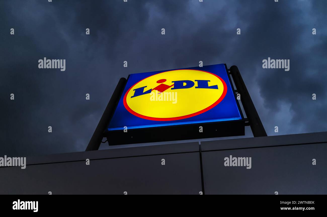 Un cartello del negozio Lidl illuminato di notte con un cielo oscuro e minaccioso. Foto Stock