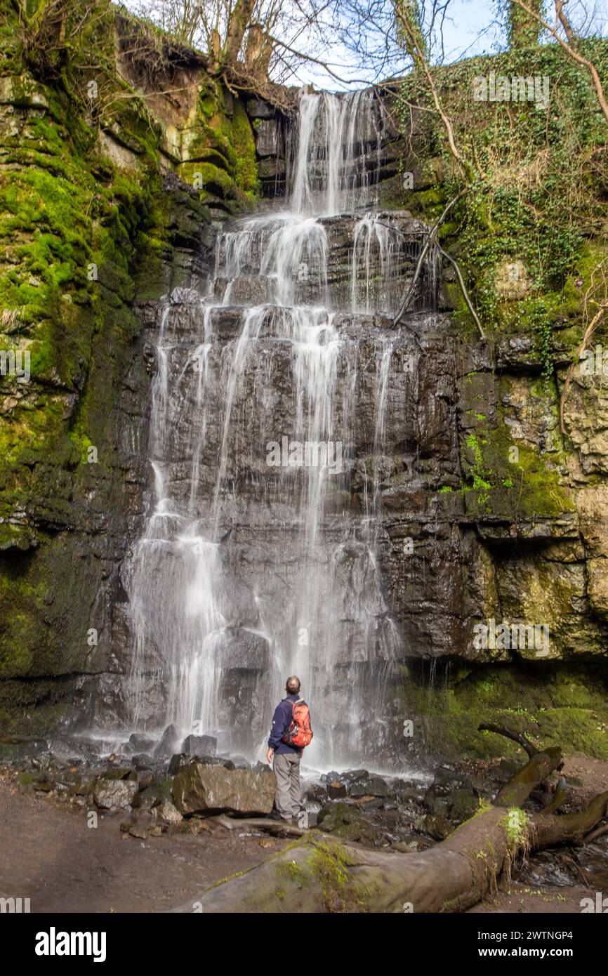 Uomo con zaino in spalla a piedi nel Peak District inglese in piedi davanti alla cascata poco conosciuta Swallet, la seconda più alta nel Derbyshire Foto Stock