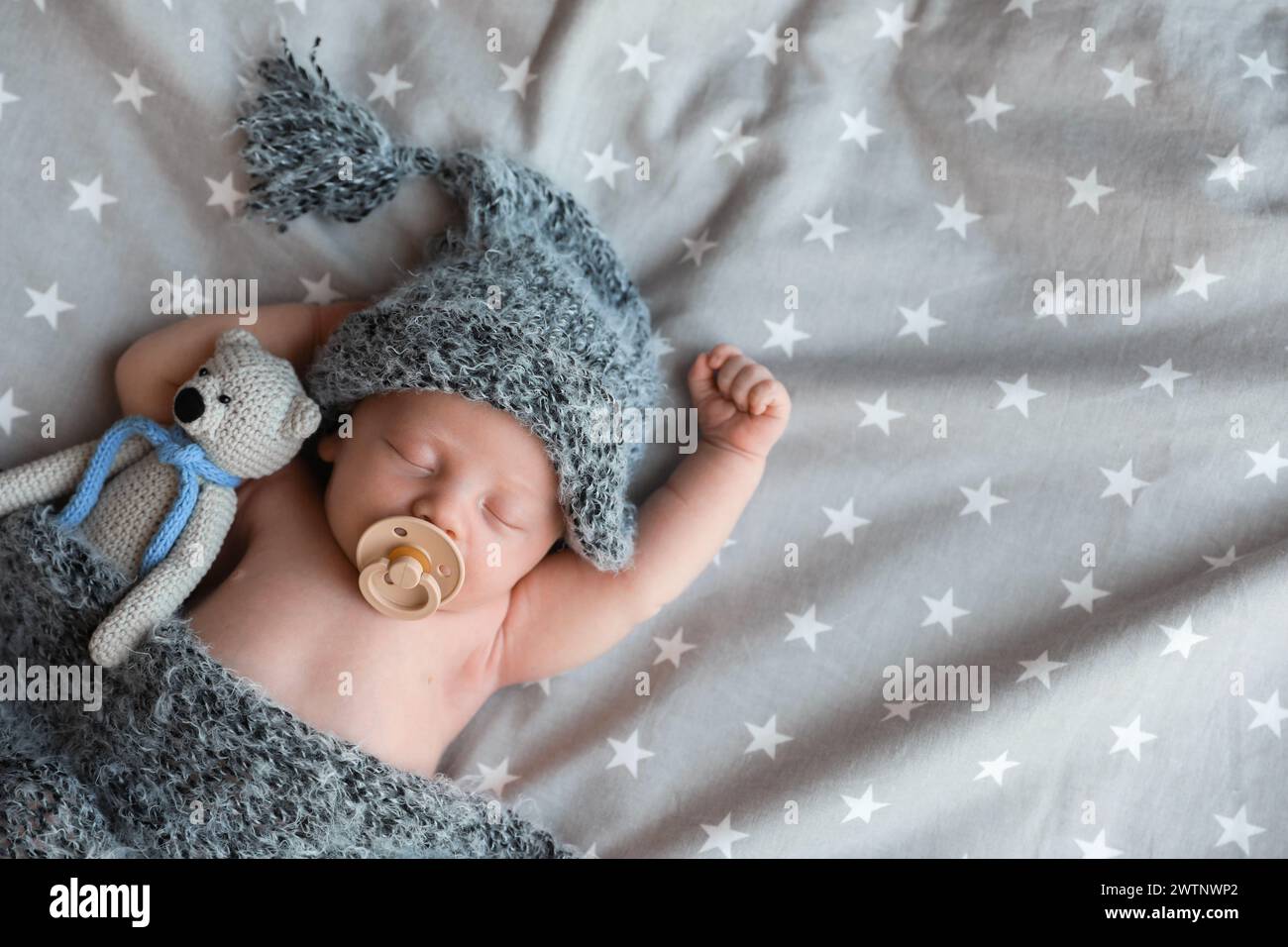 Bambino neonato carino in cappello caldo con giocattolo che dorme sul letto, vista dall'alto. Spazio per il testo Foto Stock