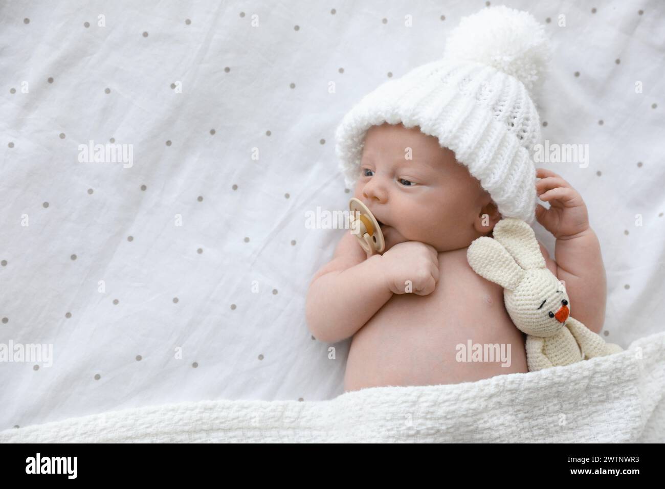 Bambino neonato carino in cappello bianco lavorato a maglia con giocattolo sdraiato sul letto, vista dall'alto. Spazio per il testo Foto Stock