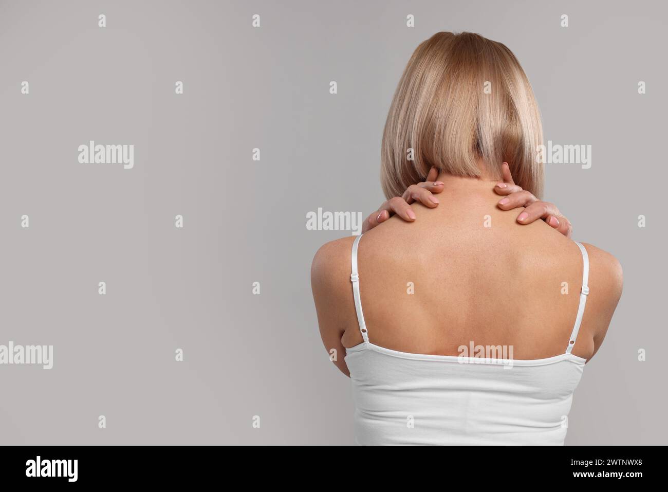 Donna che soffre di dolore al collo su sfondo grigio, vista posteriore. Spazio per il testo Foto Stock