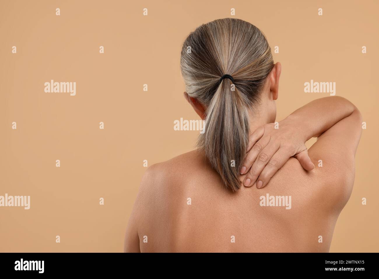 Donna matura che soffre di dolore al collo su sfondo beige, vista posteriore. Spazio per il testo Foto Stock