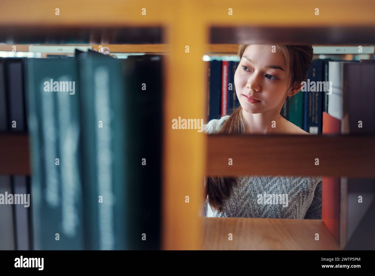 Giovane studentessa asiatica che cerca un libro sulla libreria in biblioteca. Foto Stock