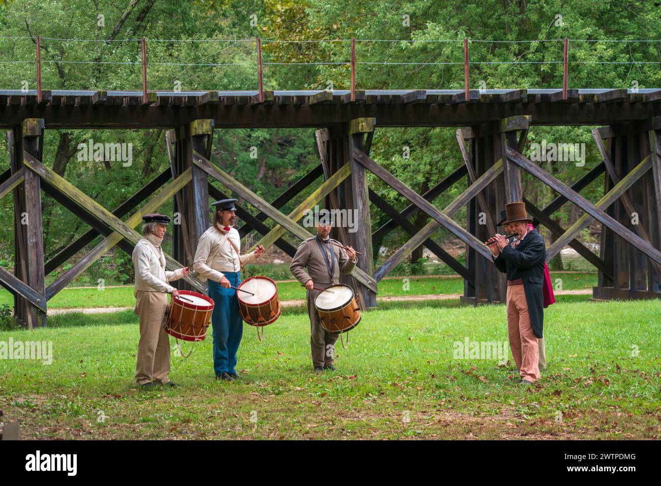 Quattro persone in abiti d'epoca si trovano su un prato tenendo tamburi davanti a un viadotto ferroviario in legno al Harpers Ferry National Historical Park. Foto Stock