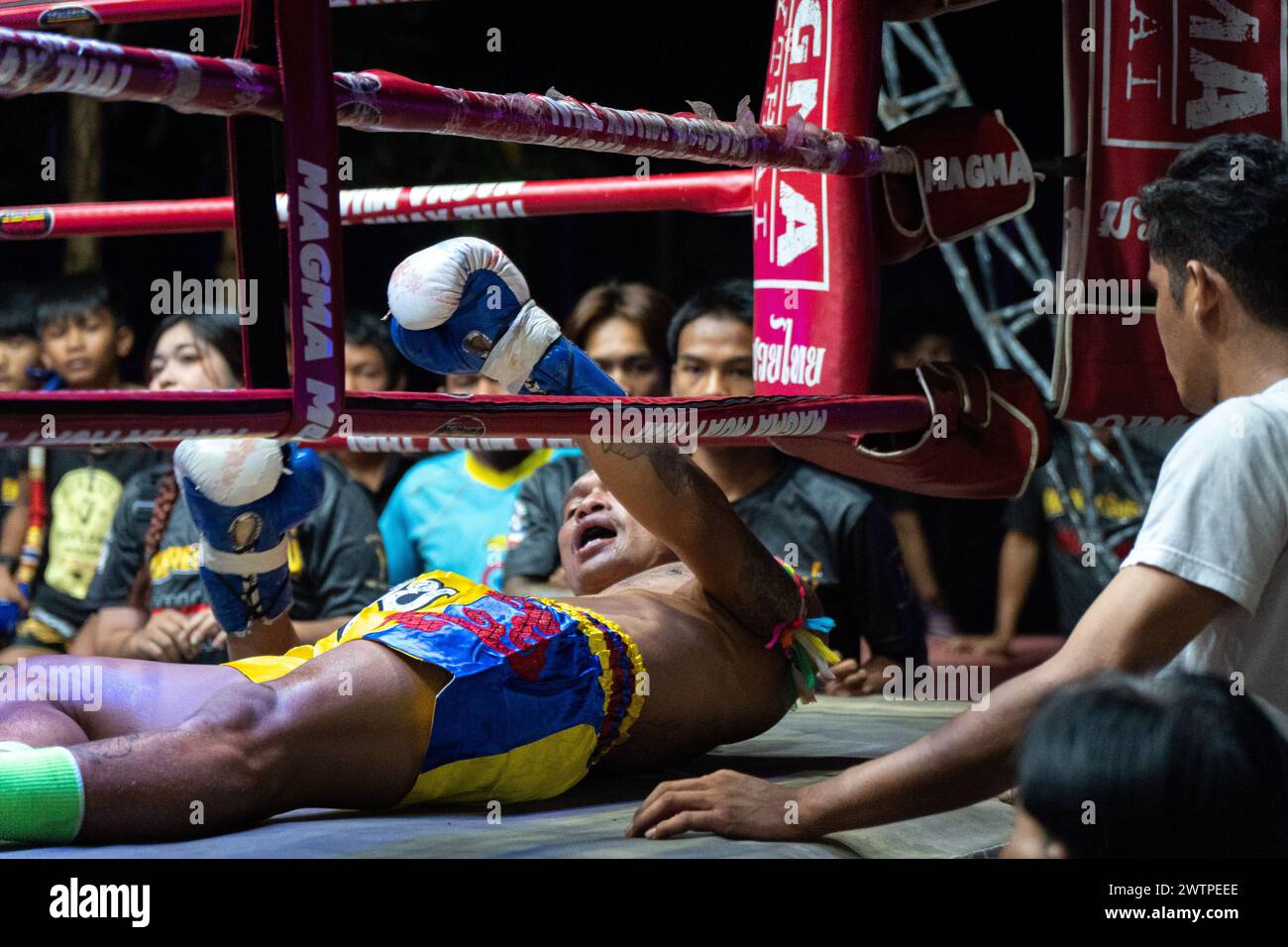 Il pugile tailandese Petch si nel, al centro, viene visto mentre tenta di sollevarsi dopo essere stato messo fuori combattimento, circondato dal pubblico, durante i combattimenti Muay Thai, sull'isola di Koh Chang, Thailandia. Foto Stock
