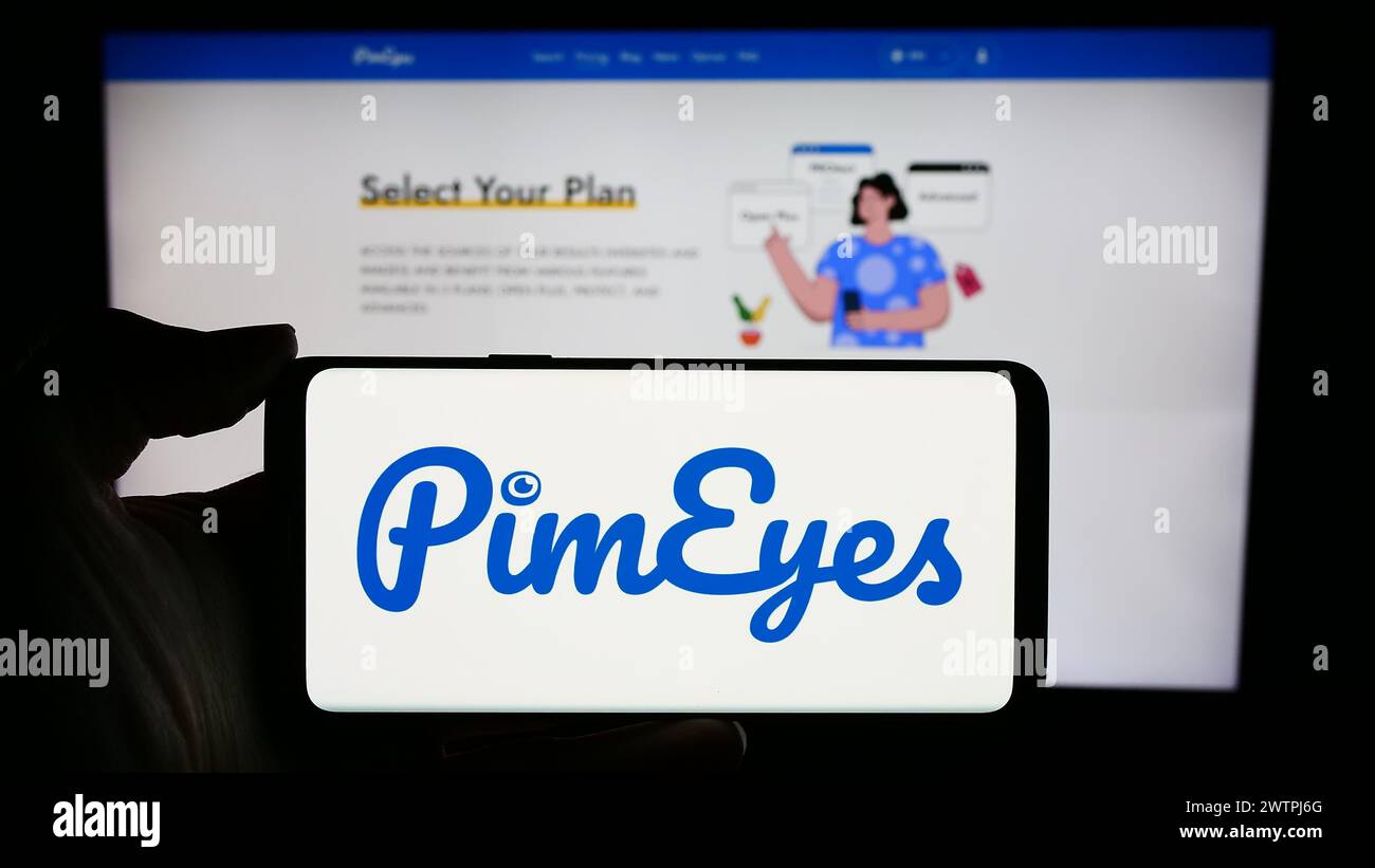 Persona che detiene un cellulare con il logo della società di ricerca per il riconoscimento facciale PimEyes di fronte alla pagina web aziendale. Mettere a fuoco il display del telefono. Foto Stock