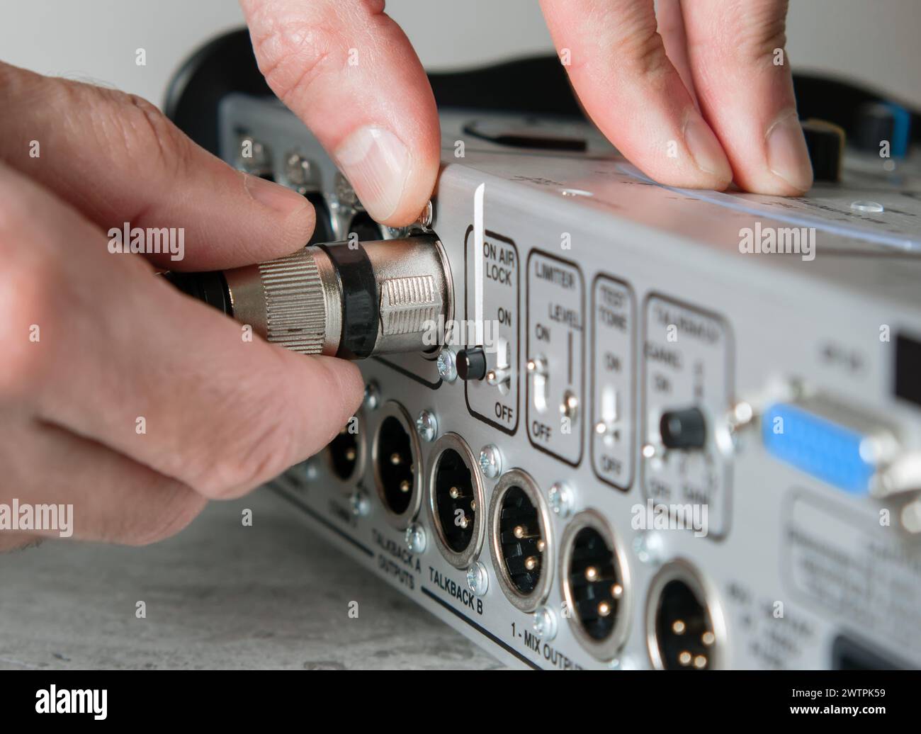 Una mano maschio scollega un cavo XLR maschio dall'ingresso di una console di miscelazione. Foto Stock