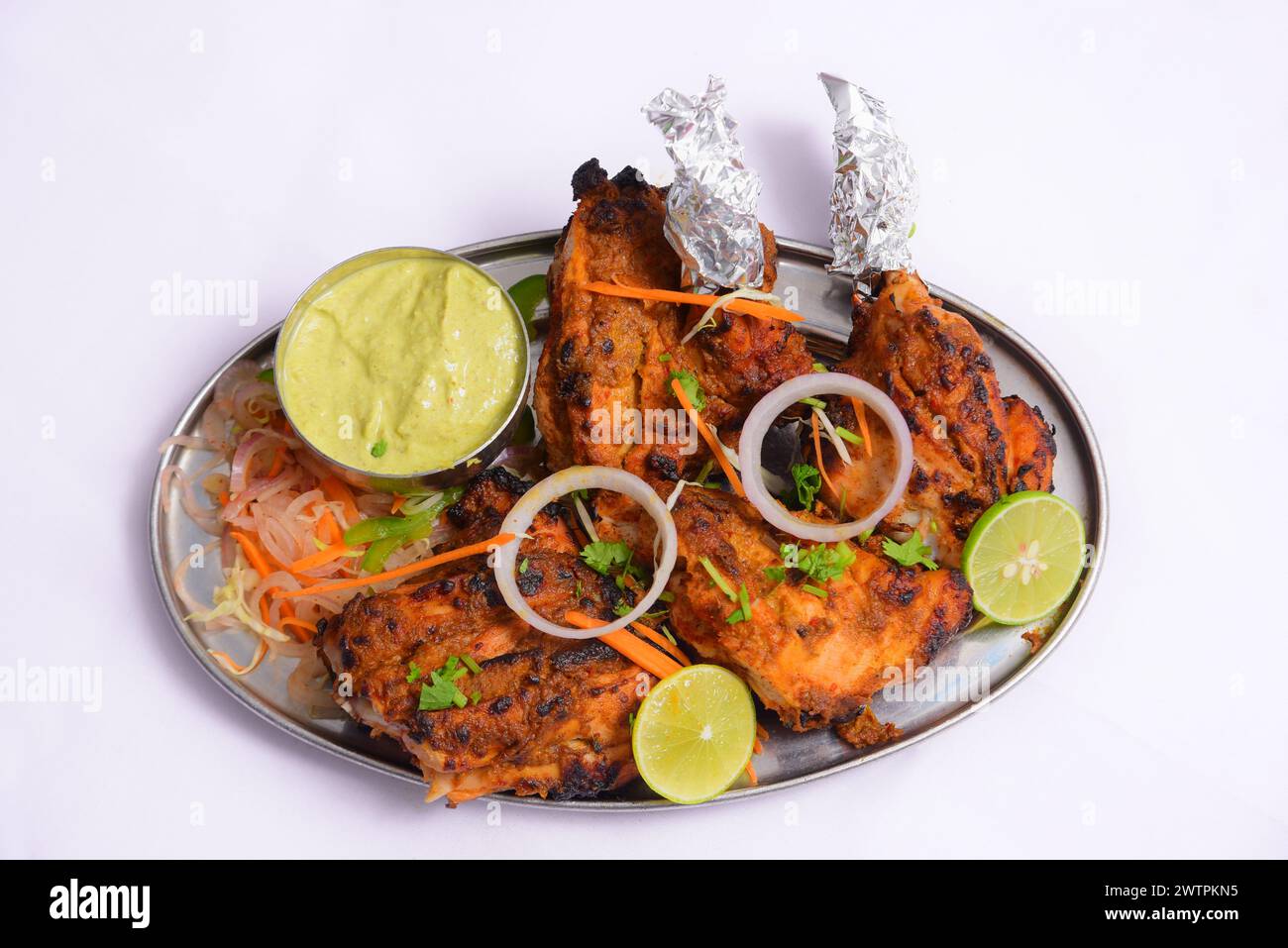Il pollo Tandoori è arrosto, marinato nello yogurt e speziato generosamente, donando alla carne un colore rosso guarnito con cipolla, limone e chutney verde Foto Stock