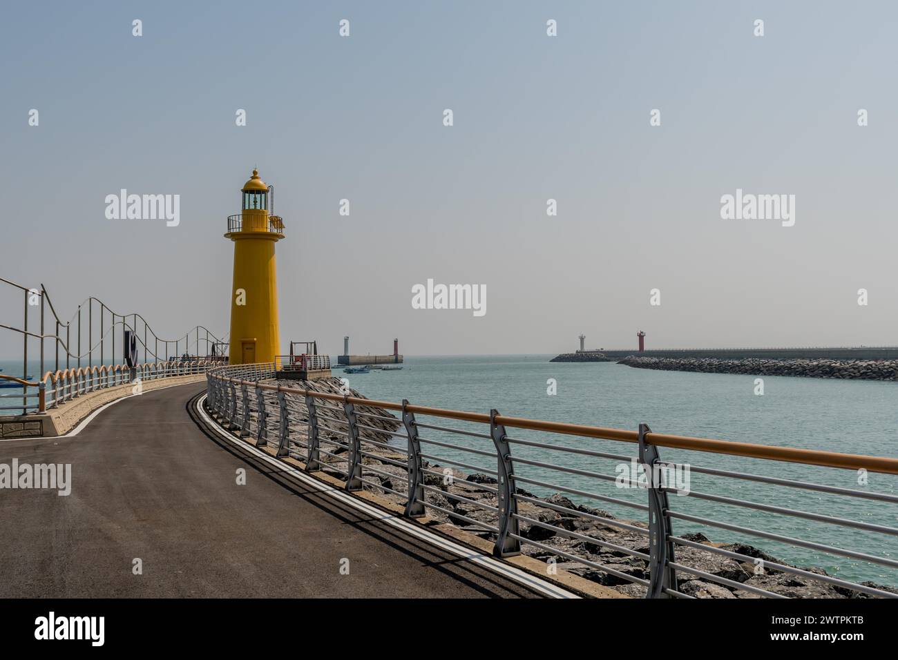 Un passaggio pedonale che conduce a un faro giallo sul mare sotto un cielo nebuloso, a Seocheon, Corea del Sud Foto Stock