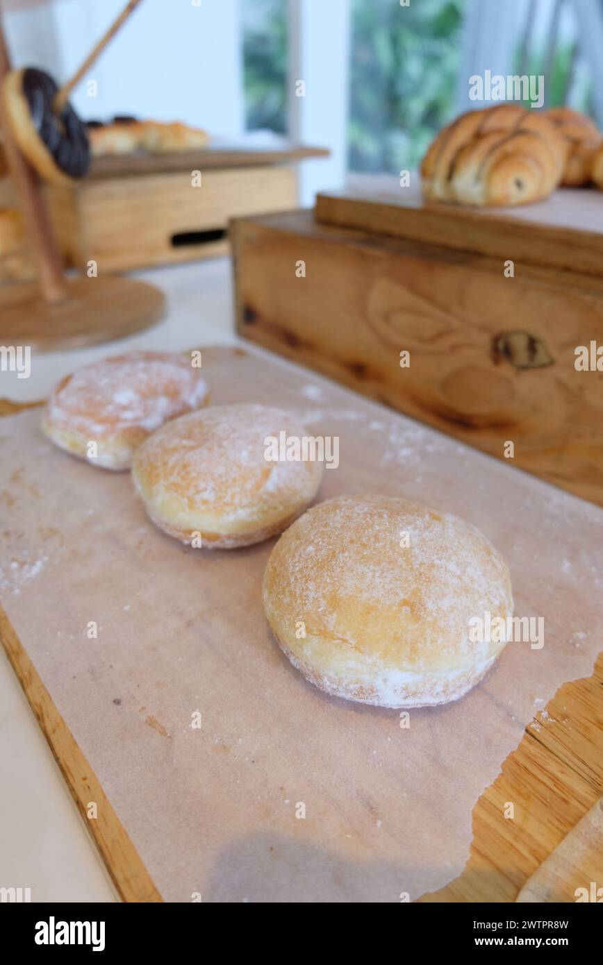 Bomboloni, krapfen o ciambelle su un tavolo di legno. Ciambelle fritte fatte in casa ripiene di crema pasticcera e condite con un velo di zucchero. Foto Stock
