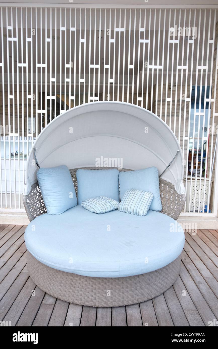 Comodo divano rotondo con biancheria blu. Divano con cuscino nel giardino esterno. Divisore per ambienti estetici sul lato posteriore. Foto Stock
