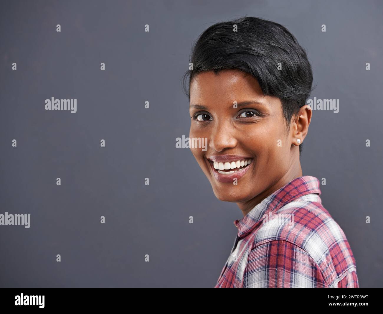 Felice, ritratto e indiano con sorriso e sfondo grigio presso un ufficio di agenzia creativa. Hipster, confidenza e dipendente non binario con il moderno Foto Stock