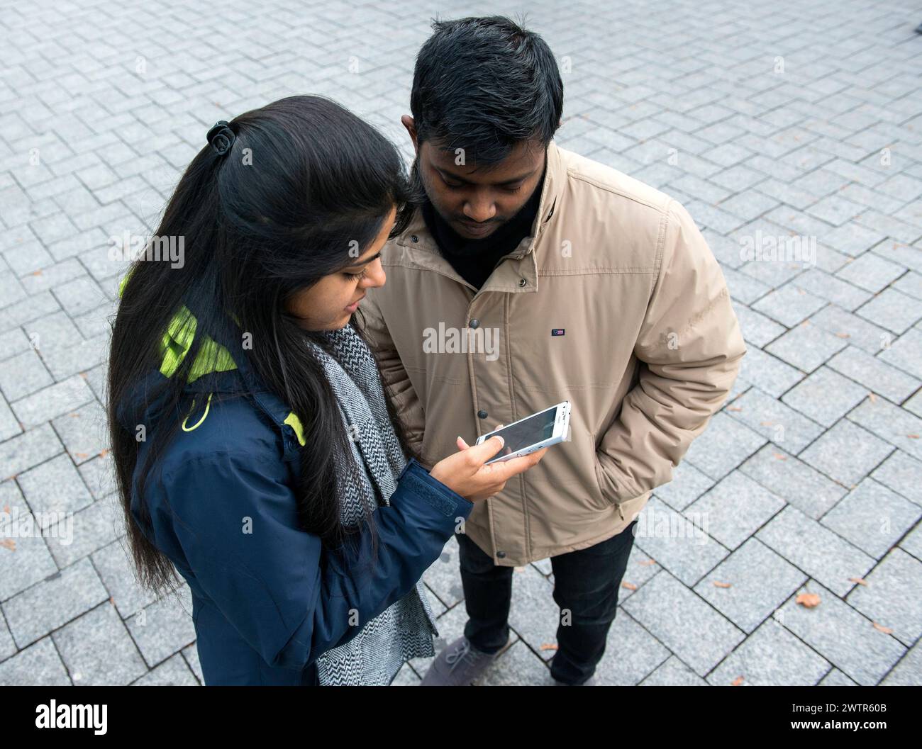 Una coppia che naviga in una città di Aquisgrana, Germania. Giovane coppia indiana di studenti universitari che si scambiano per esplorare la loro nuova città utilizzando un'applicazione per la mappa dello smartphone. MRYES Aachen Centrum Nortrhein-Westfalen Duitsland Copyright: XGuidoxKoppesx Foto Stock