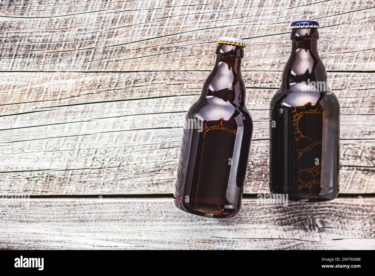 Due bottiglie di vetro marrone riempite di birra sono collocate ordinatamente sopra un tavolo di legno. Foto Stock
