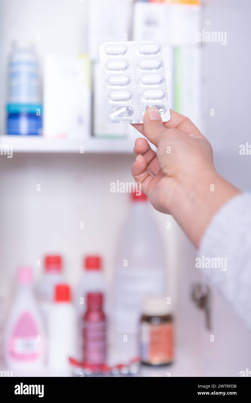 Mano di una persona irriconoscibile, prendendo la medicina necessaria dal gabinetto di medicina a casa. Foto Stock