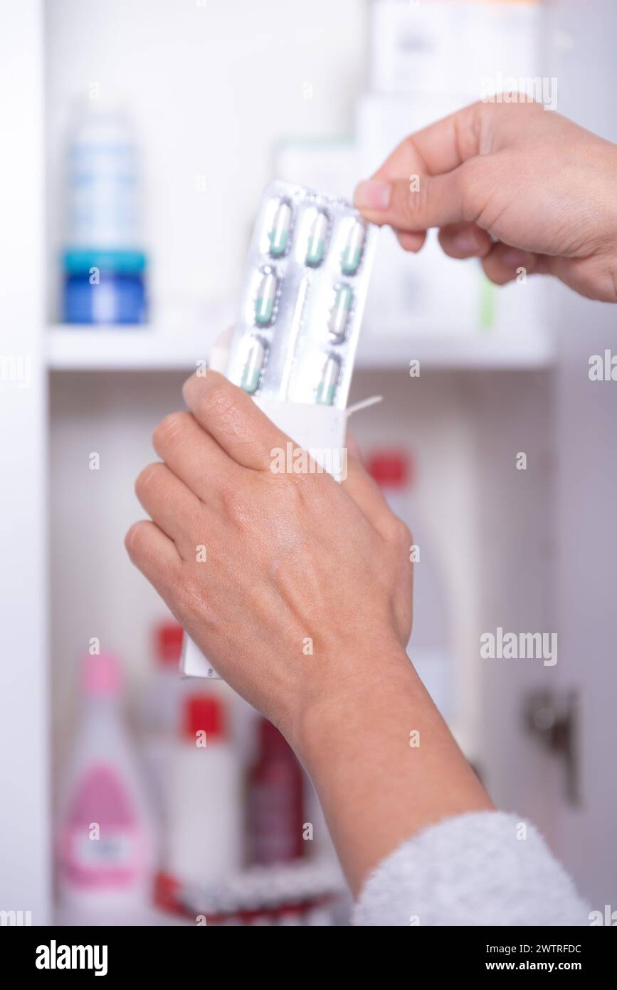 Mano di una persona irriconoscibile, prendendo la medicina necessaria dal gabinetto di medicina a casa. Foto Stock