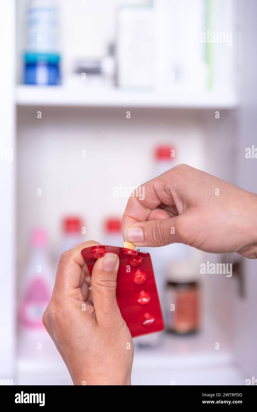 Mano di una persona irriconoscibile, prendendo la medicina necessaria dal gabinetto di medicina a casa. Foto Stock