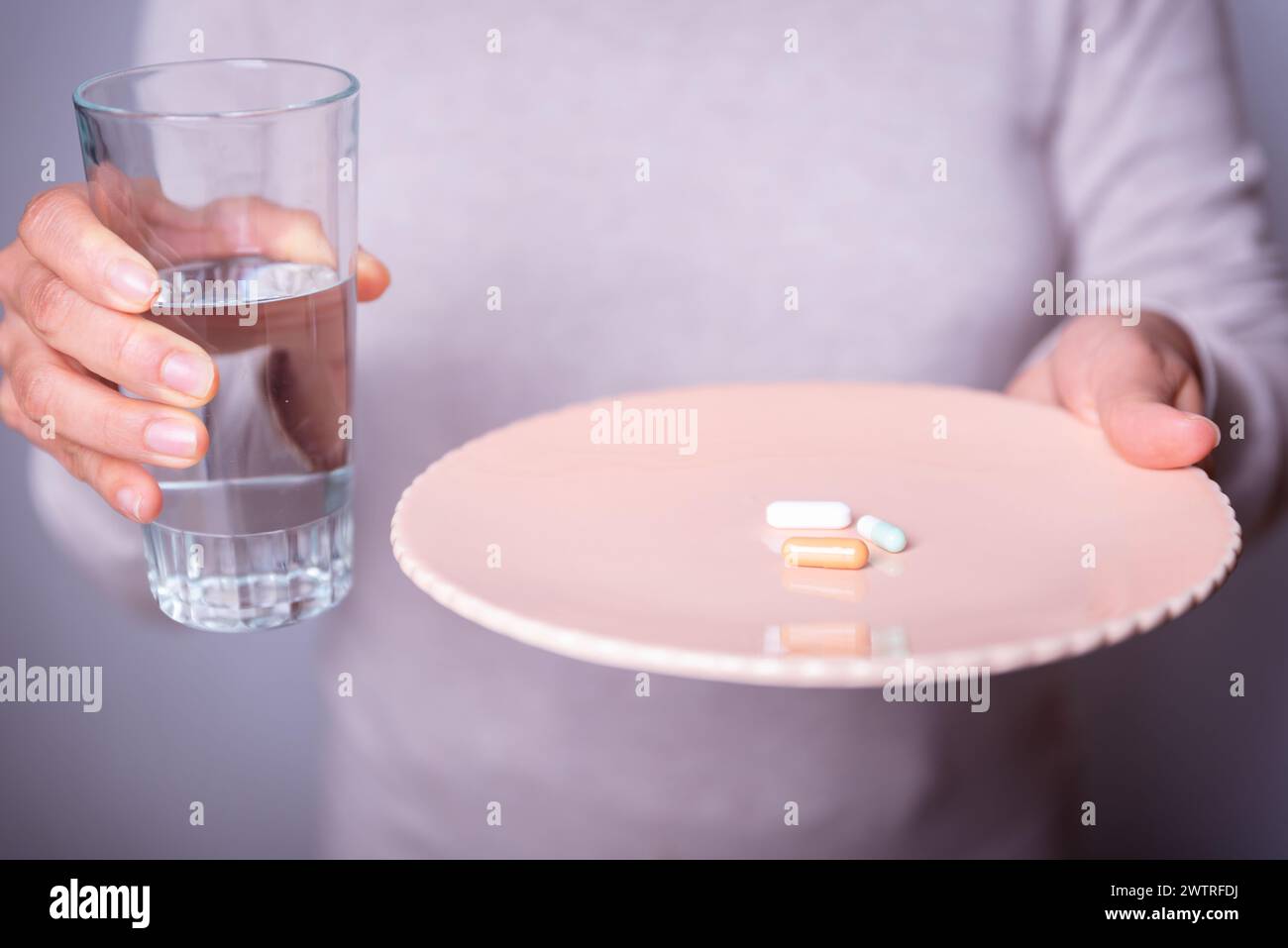Persona irriconoscibile con un piatto di pillole e un bicchiere d'acqua. Foto Stock