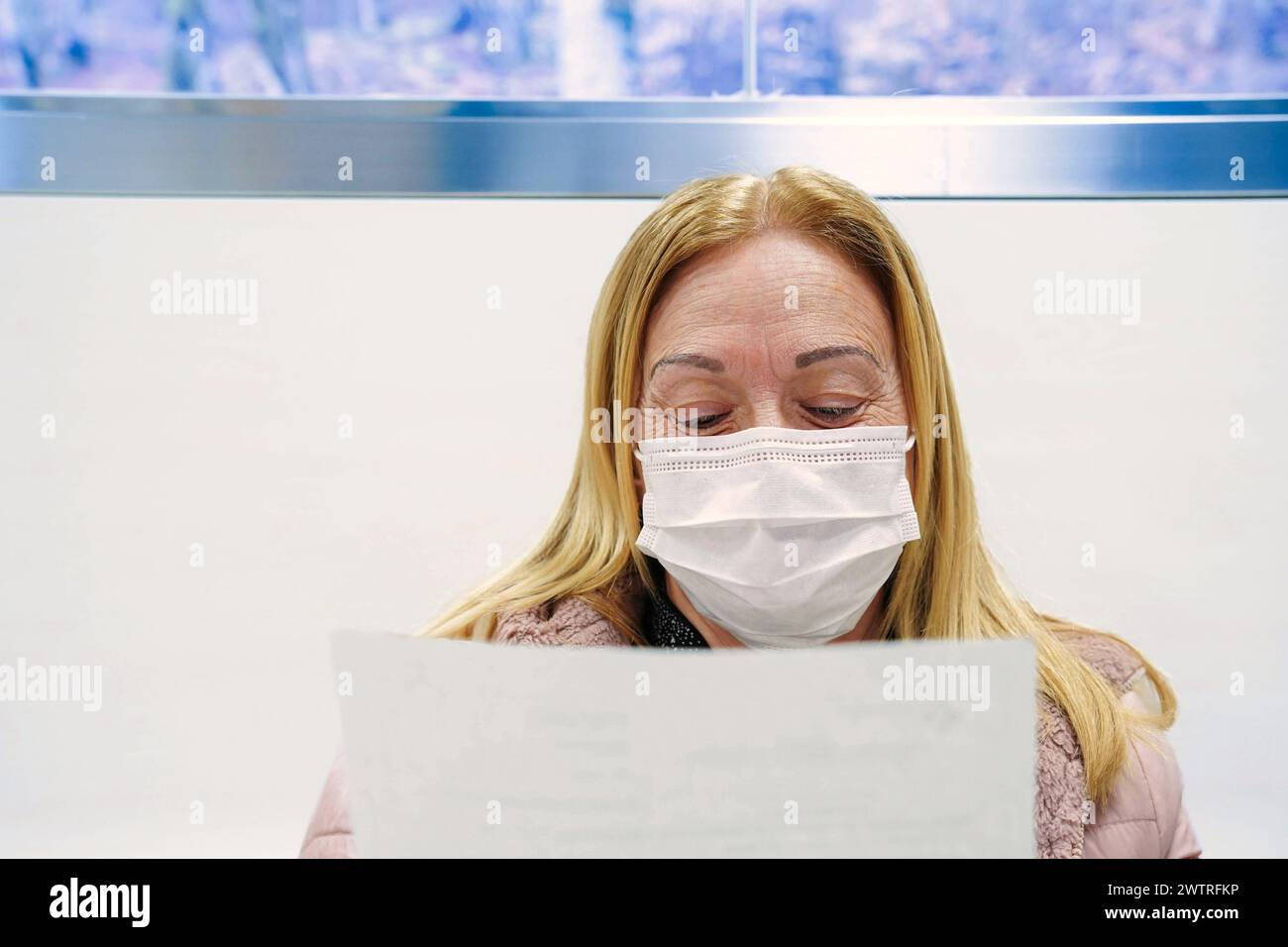 Una donna che indossa una maschera che legge un documento sanitario nella sala d'attesa di un ospedale. Giornata della salute Foto Stock