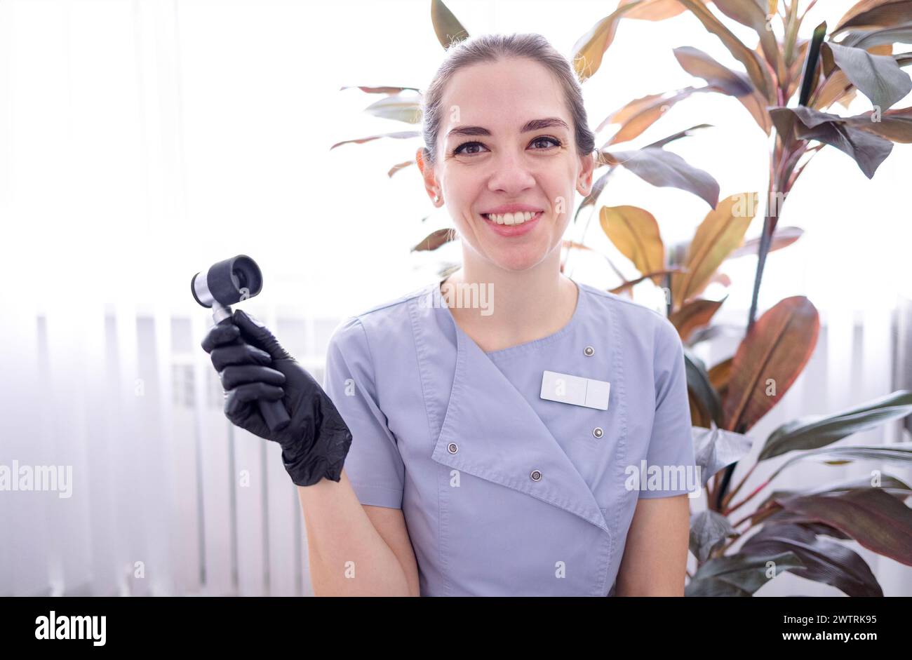 Una giovane donna in uniforme da medico e guanti neri con un dermatoscopio in mano in un salone di bellezza. Un dermatologo sorridente con uno strumento che esamina Foto Stock