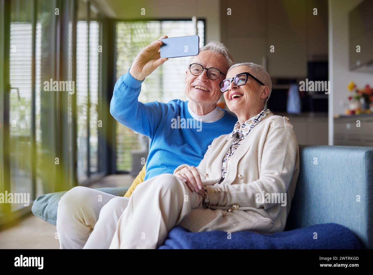 Felice coppia anziana seduta sul divano a casa a fare selfie Foto Stock