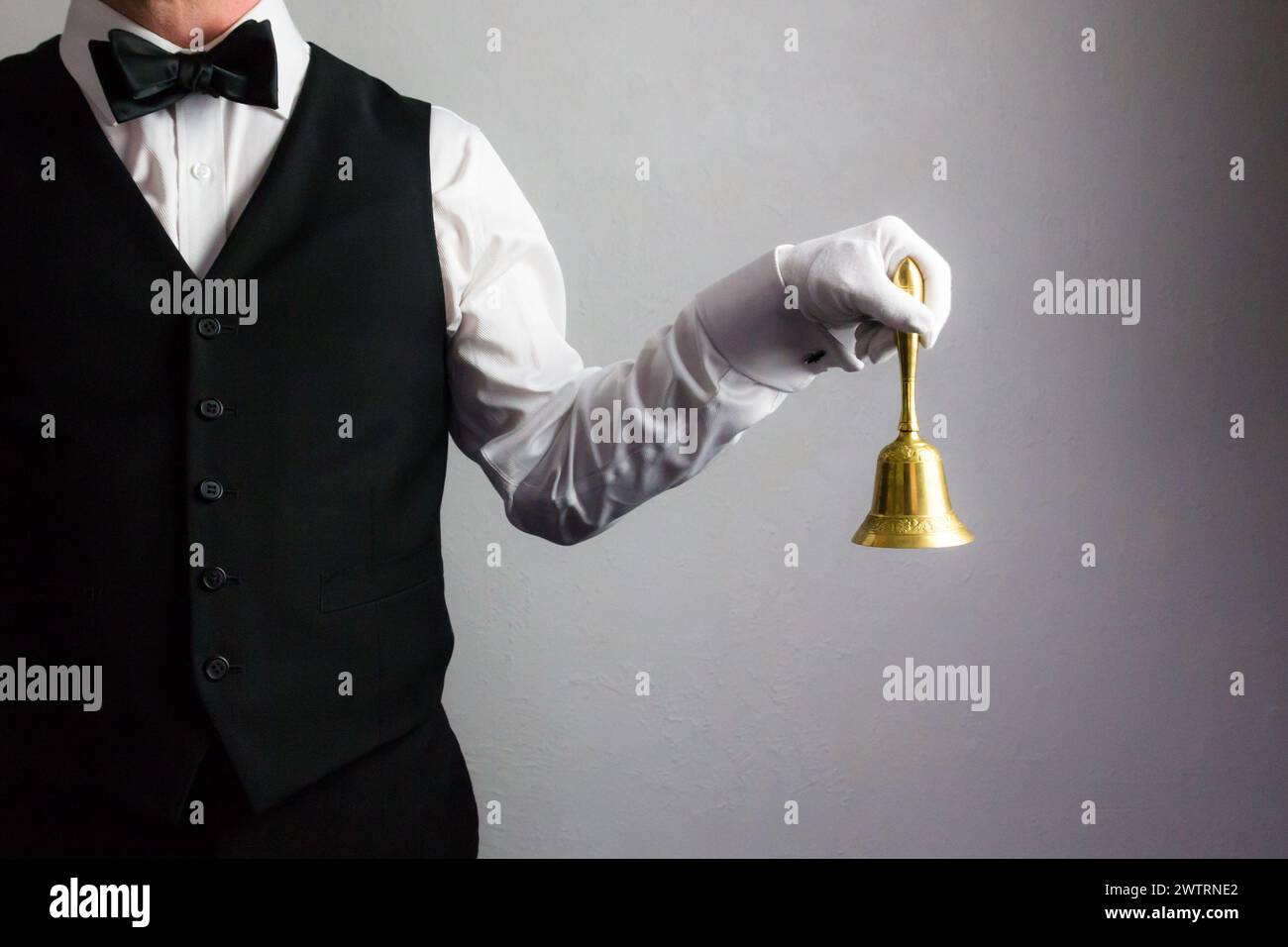 Maggiordomo o cameriere con gilet nero e cravatta con fiocco e guanti bianchi con campana d'oro. Suoneria per assistenza. Foto Stock