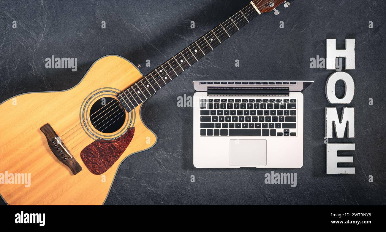 Chitarra acustica, laptop e parola decorativa Home su sfondo scuro, vista dall'alto. Foto Stock