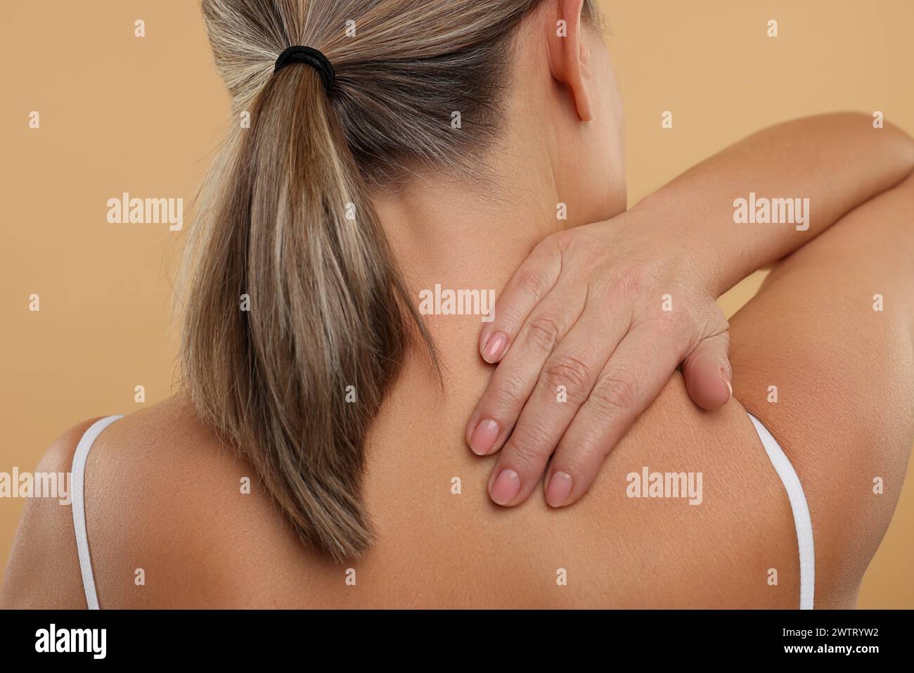 Donna matura che soffre di dolore al collo su sfondo beige, vista posteriore Foto Stock