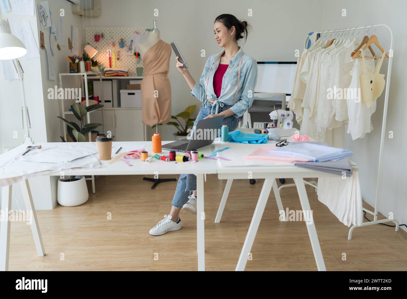 Imprenditrice che guarda un tablet in uno studio di sartoria, è una designer tessile che produce nuove collezioni utilizzando tecnologie all'avanguardia. Foto Stock