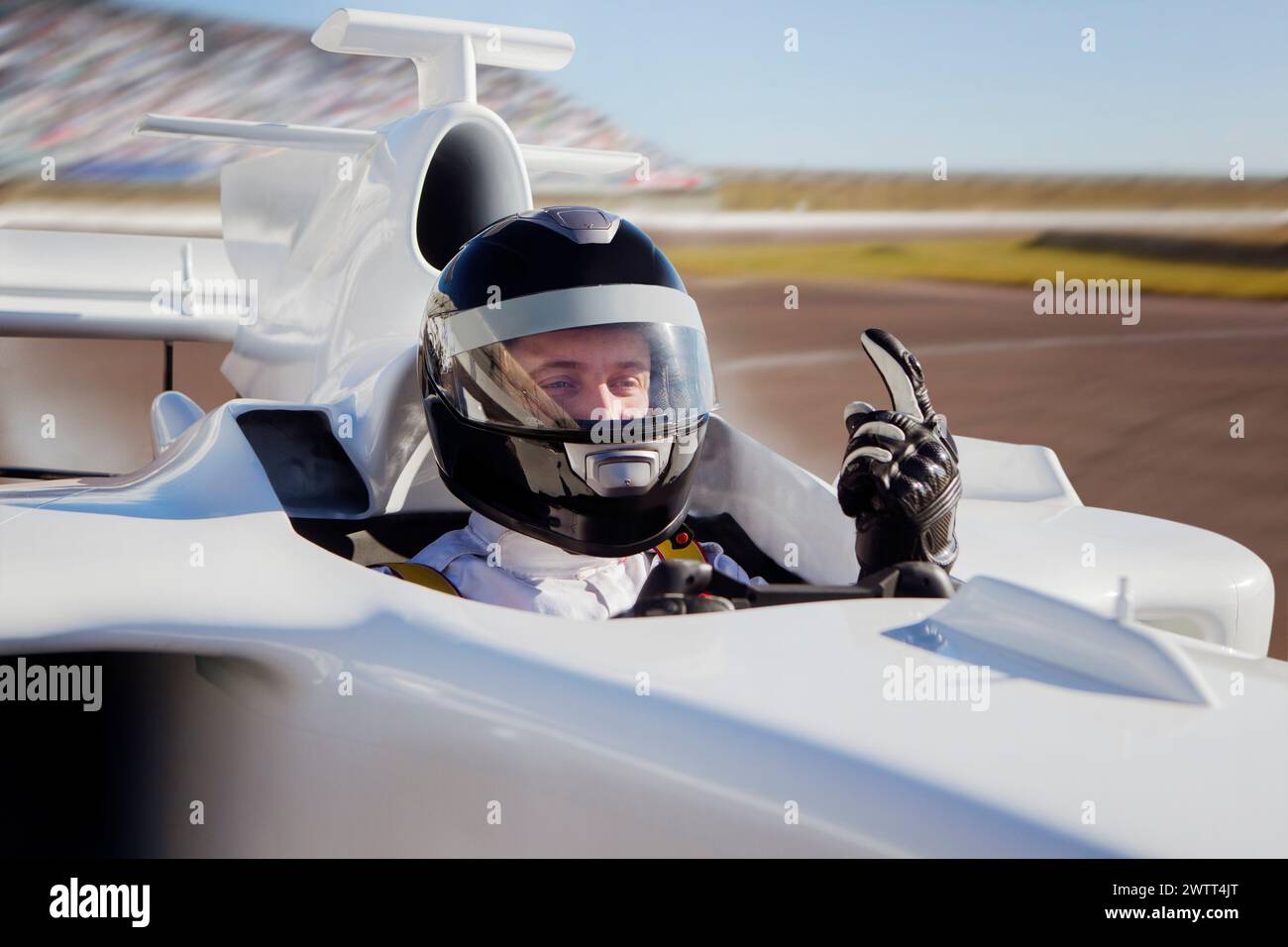 Pilota di auto da corsa che regala un pollice dalla cabina di pilotaggio di un veicolo ad alta velocità in pista. Foto Stock
