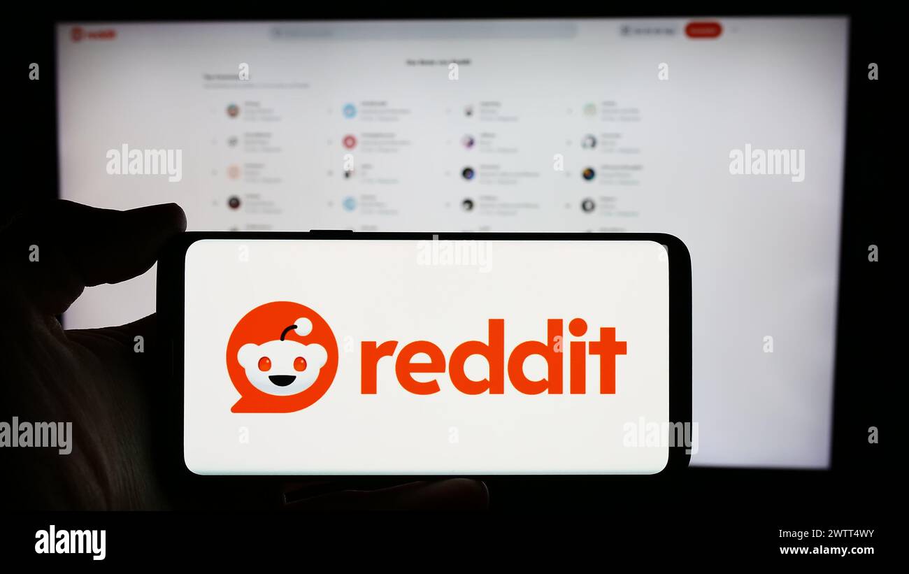 Persona che detiene un cellulare con il logo della società di social media statunitense Reddit Inc. Di fronte alla pagina Web aziendale. Mettere a fuoco il display del telefono. Foto Stock