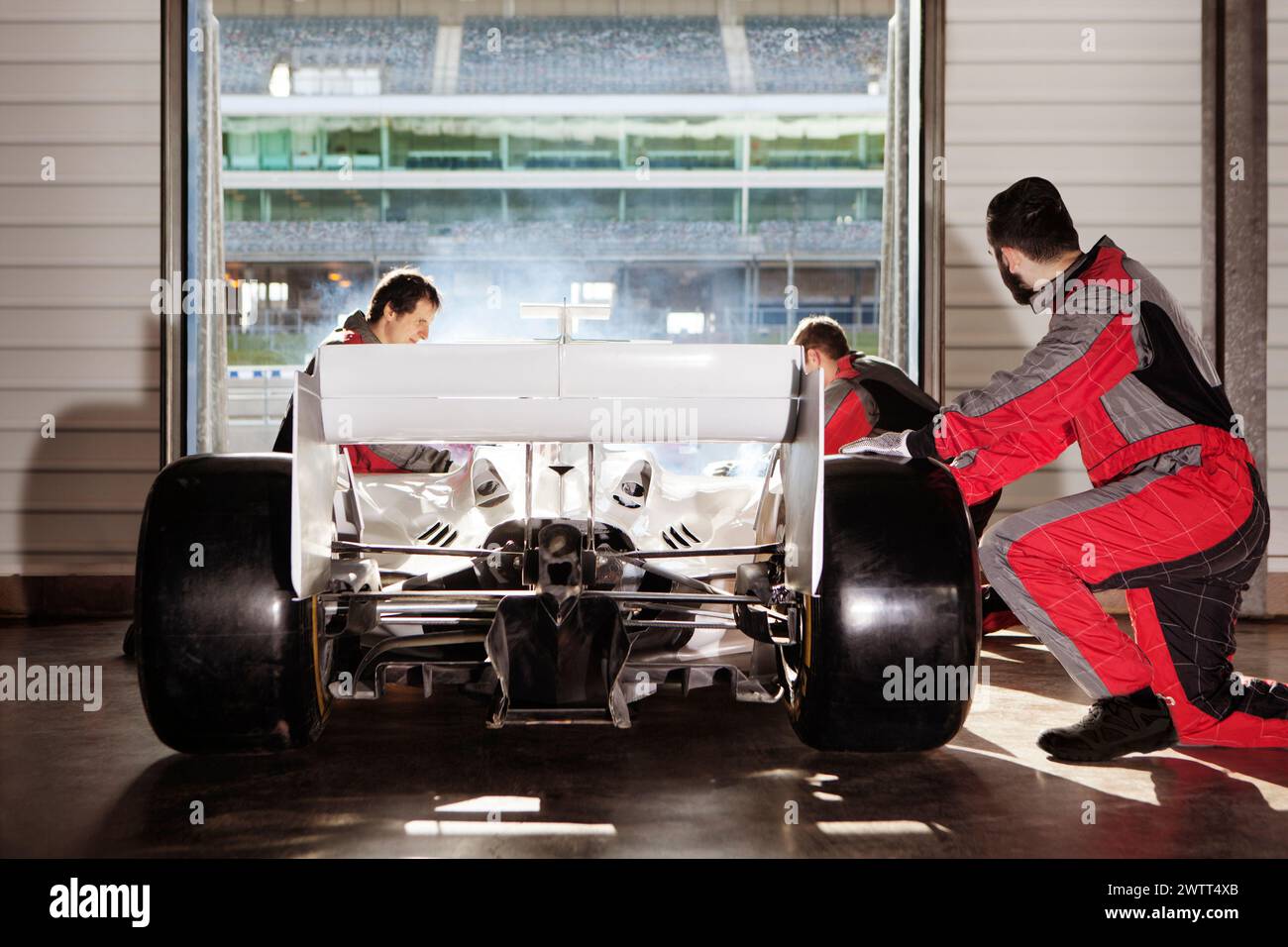 Lavoro di squadra nel garage delle corse mentre i meccanici mettono a punto un'auto da corsa ad alte prestazioni. Foto Stock