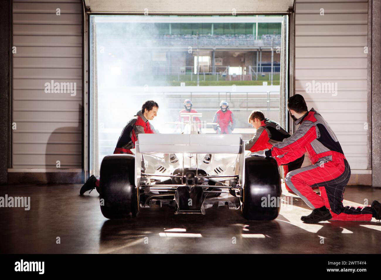 Team di pit crew che lavora su un'auto da corsa in un garage sullo sfondo di una pista illuminata dal sole Foto Stock