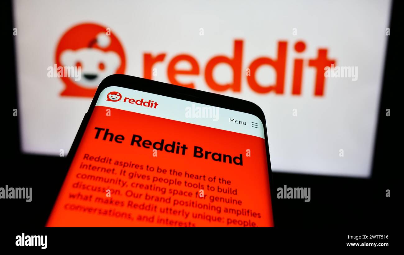 Telefono cellulare con sito web della società di social media statunitense Reddit Inc. Davanti al logo aziendale. Mettere a fuoco in alto a sinistra sul display del telefono. Foto Stock