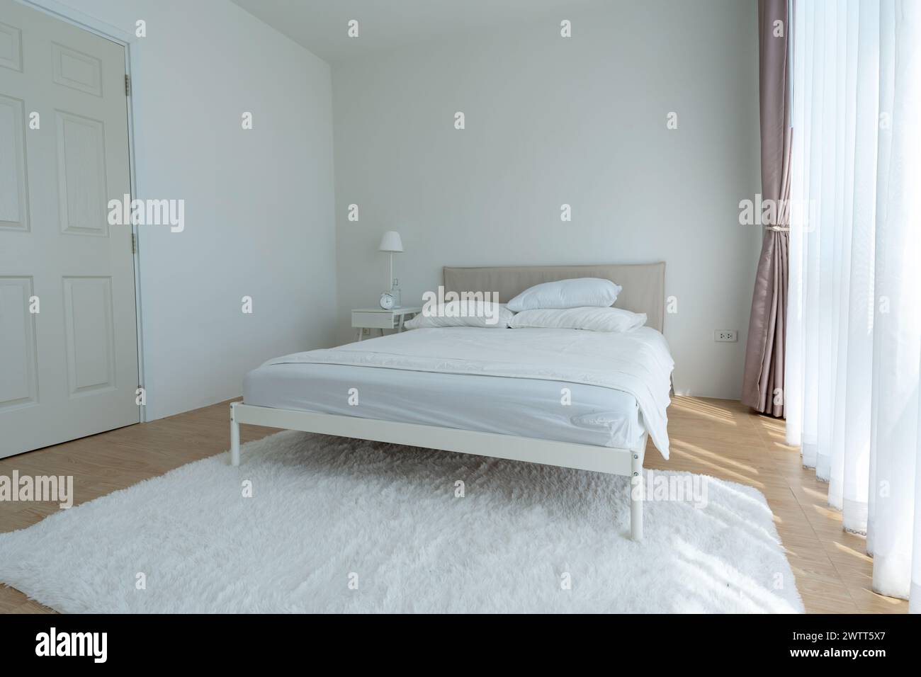 Camera da letto bianca con tende bianche e cuscini bianchi la mattina Foto Stock