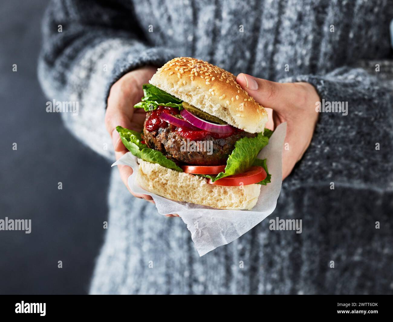 Primo piano di mani che tengono in mano un succoso hamburger pronto da mangiare. Foto Stock