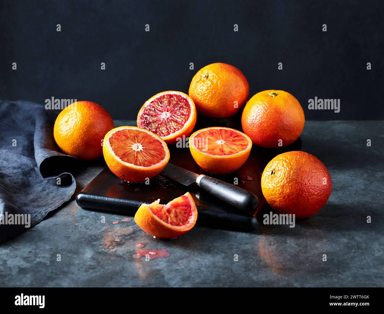 Le arance di sangue sono tagliate a fette su una superficie di cucina scura Foto Stock