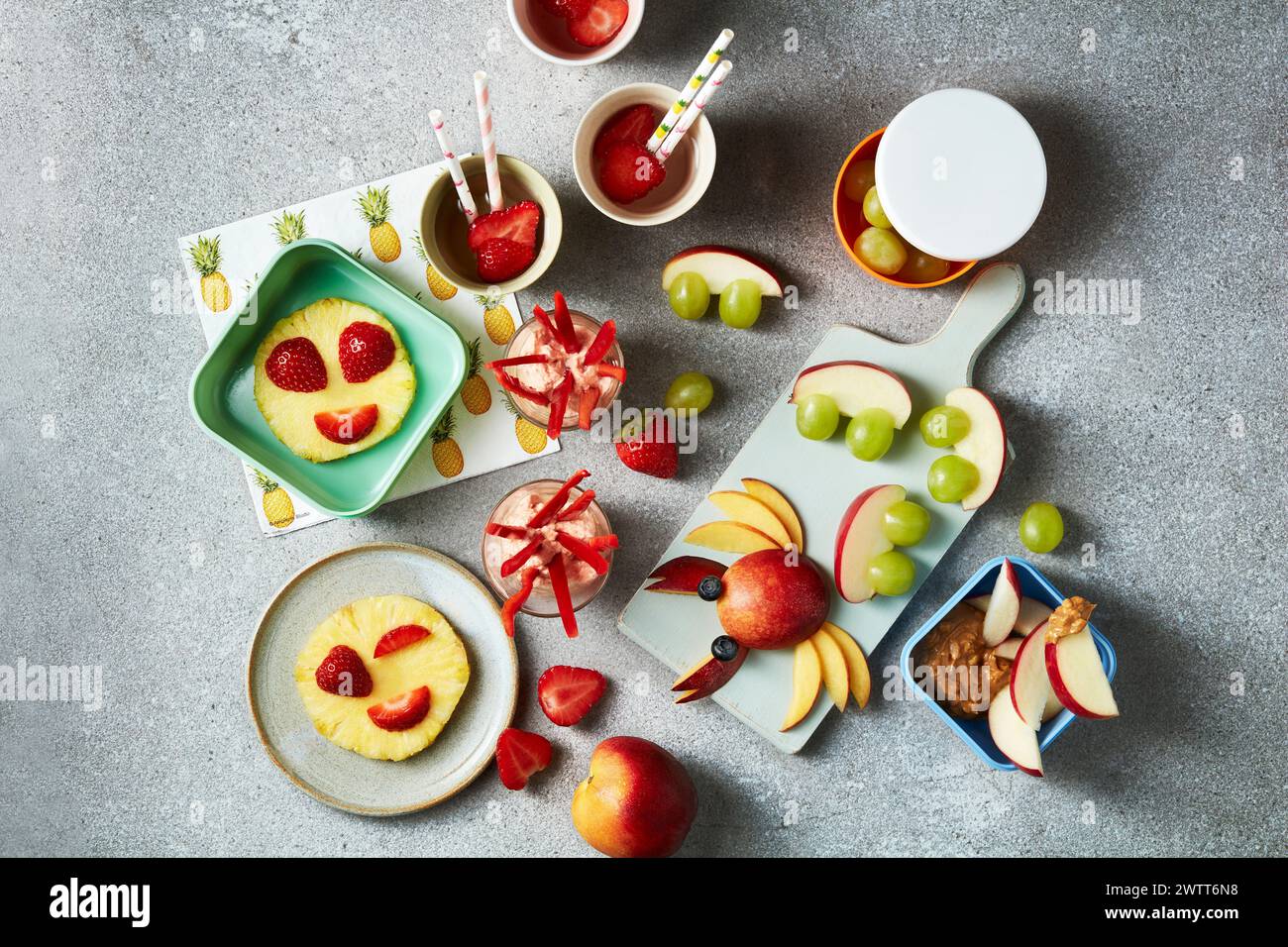 Una colorata esposizione di spuntini sani con facce di frutta su sfondo grigio testurizzato. Foto Stock