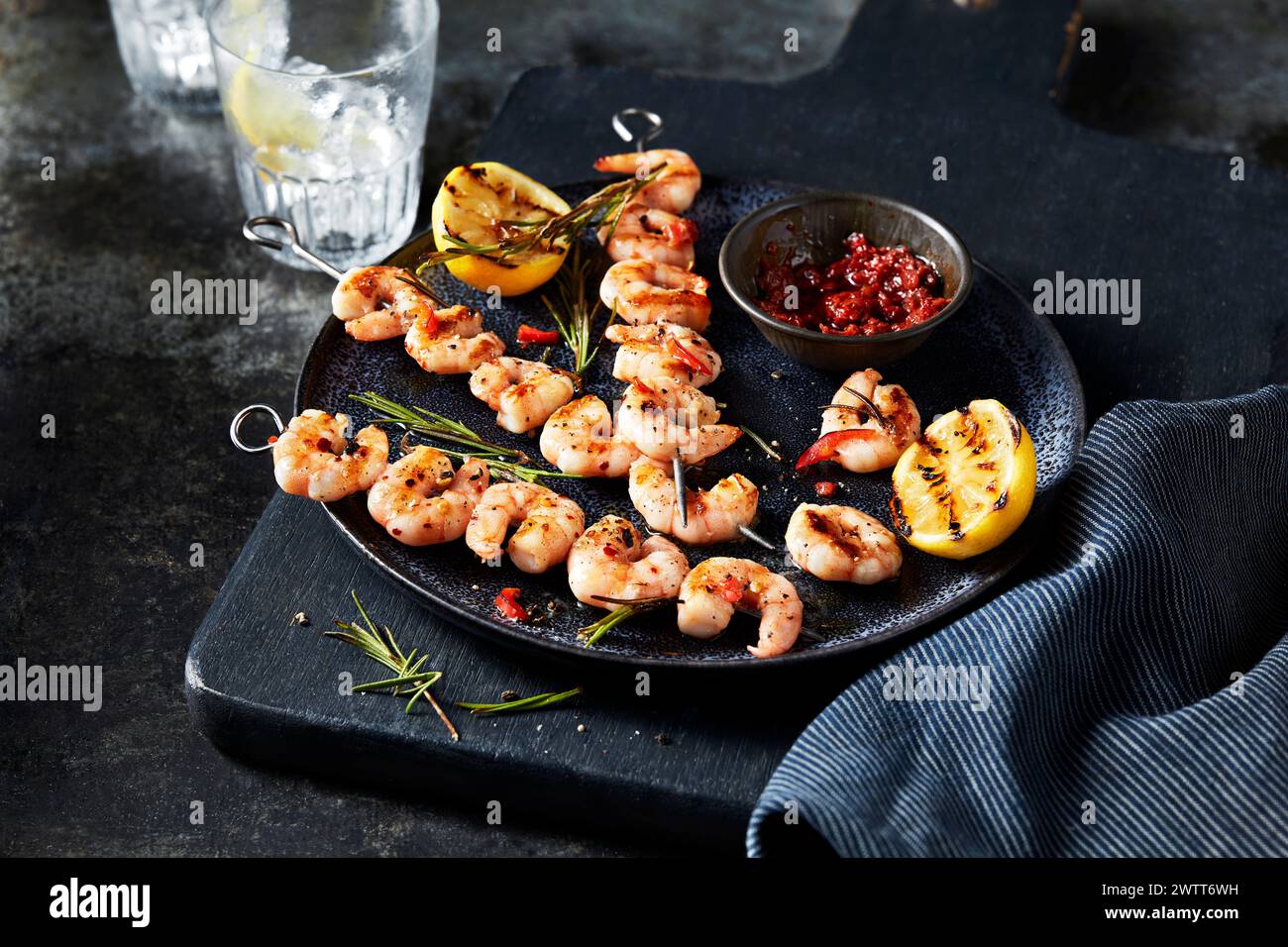 Spiedini di gamberi grigliati con limone e salsa per immersione su un tavolo rustico e scuro. Foto Stock