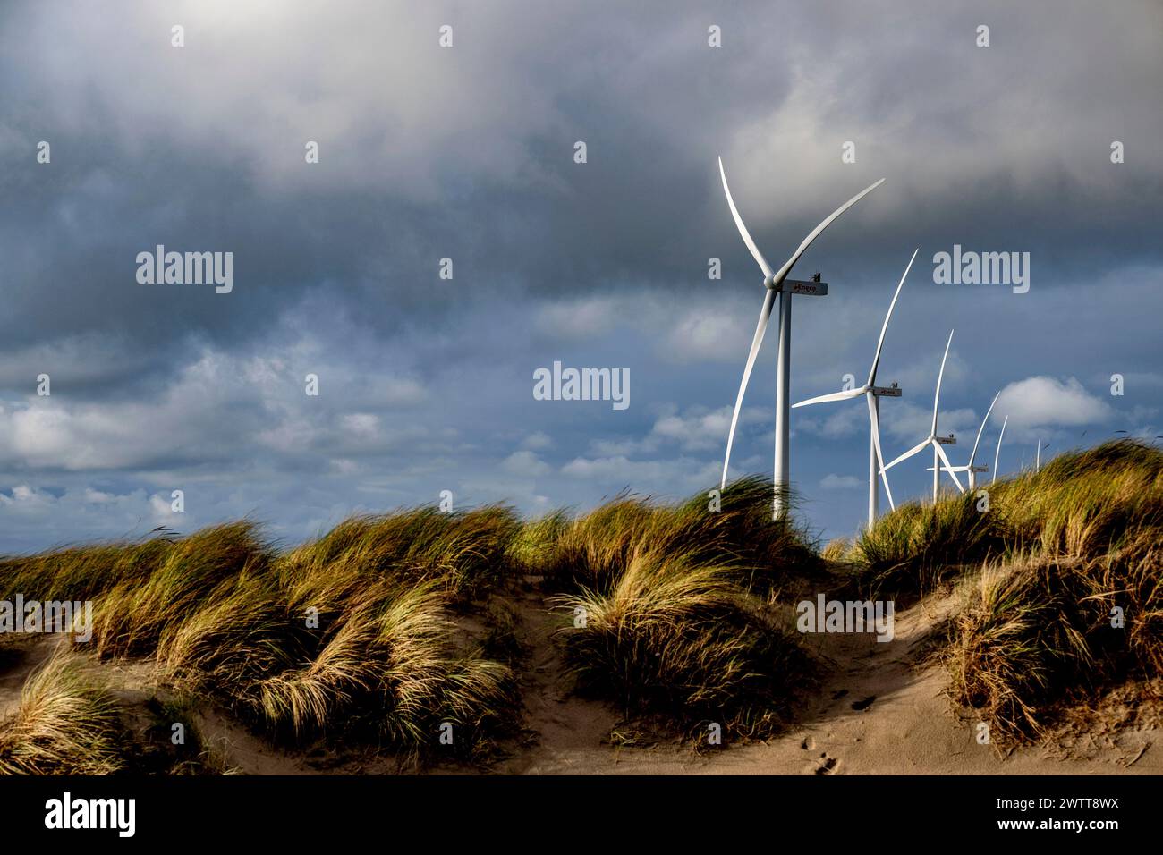 Turbine eoliche alte in mezzo a un cielo spettacolare e dune battute dal vento Foto Stock