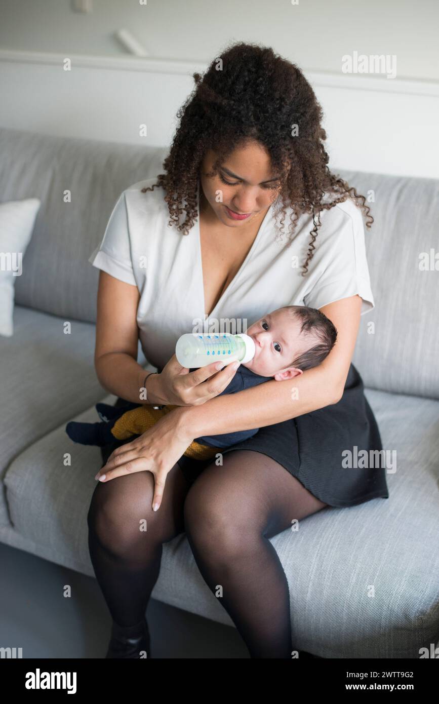Un momento tenero come una madre nutre il suo bambino sul divano. Foto Stock