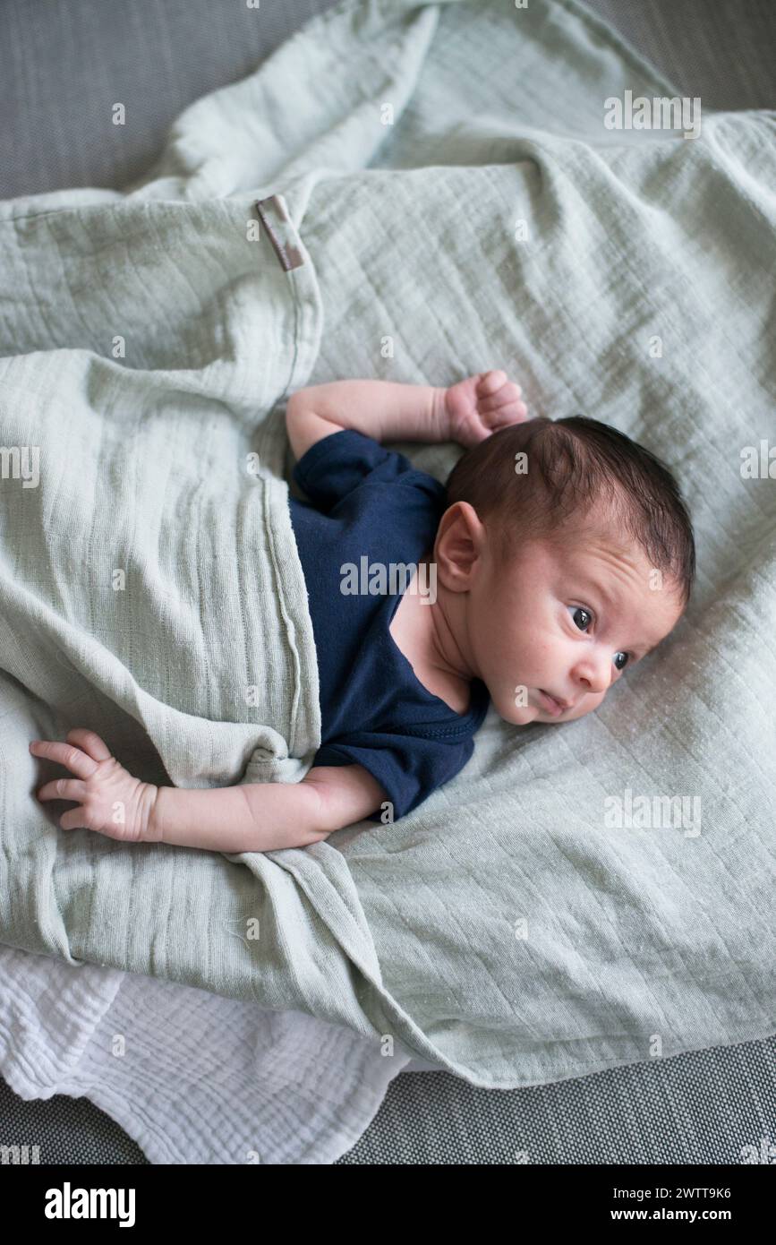 Un bambino curioso giace su una coperta morbida, guardando il mondo che li circonda. Foto Stock