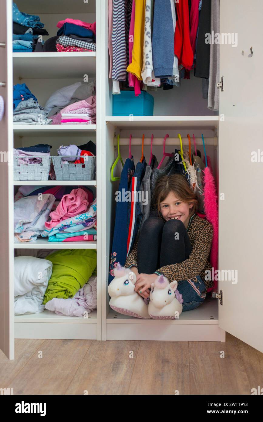 Giovane ragazza che si gode un momento di gioco nascosto in un guardaroba pieno di vestiti. Foto Stock