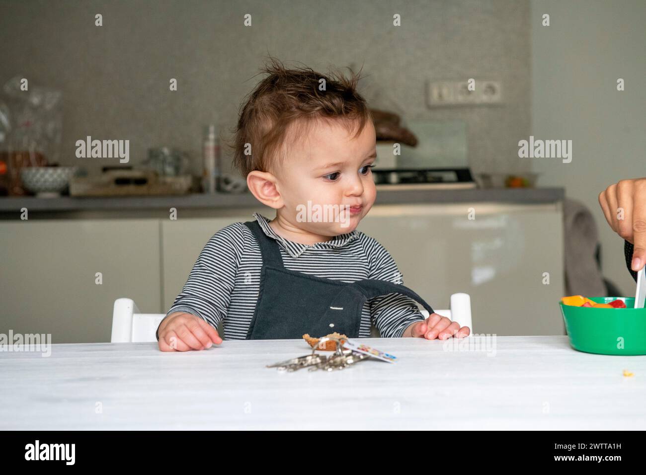 Bambino piccolo con uno sguardo curioso al tavolo da pranzo Foto Stock