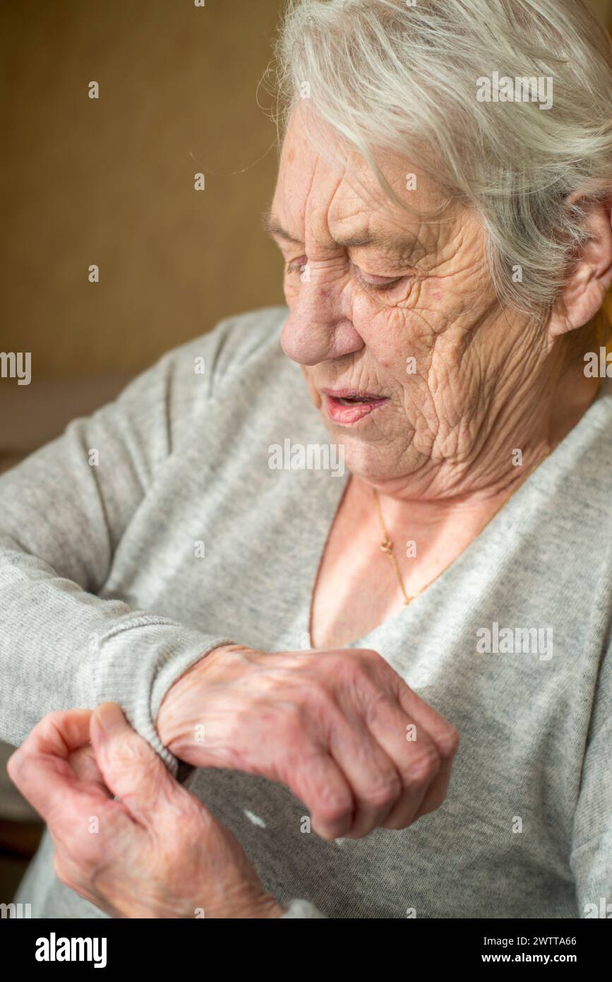 Donna anziana che ispeziona delicatamente le mani con uno sguardo di contemplazione. Foto Stock