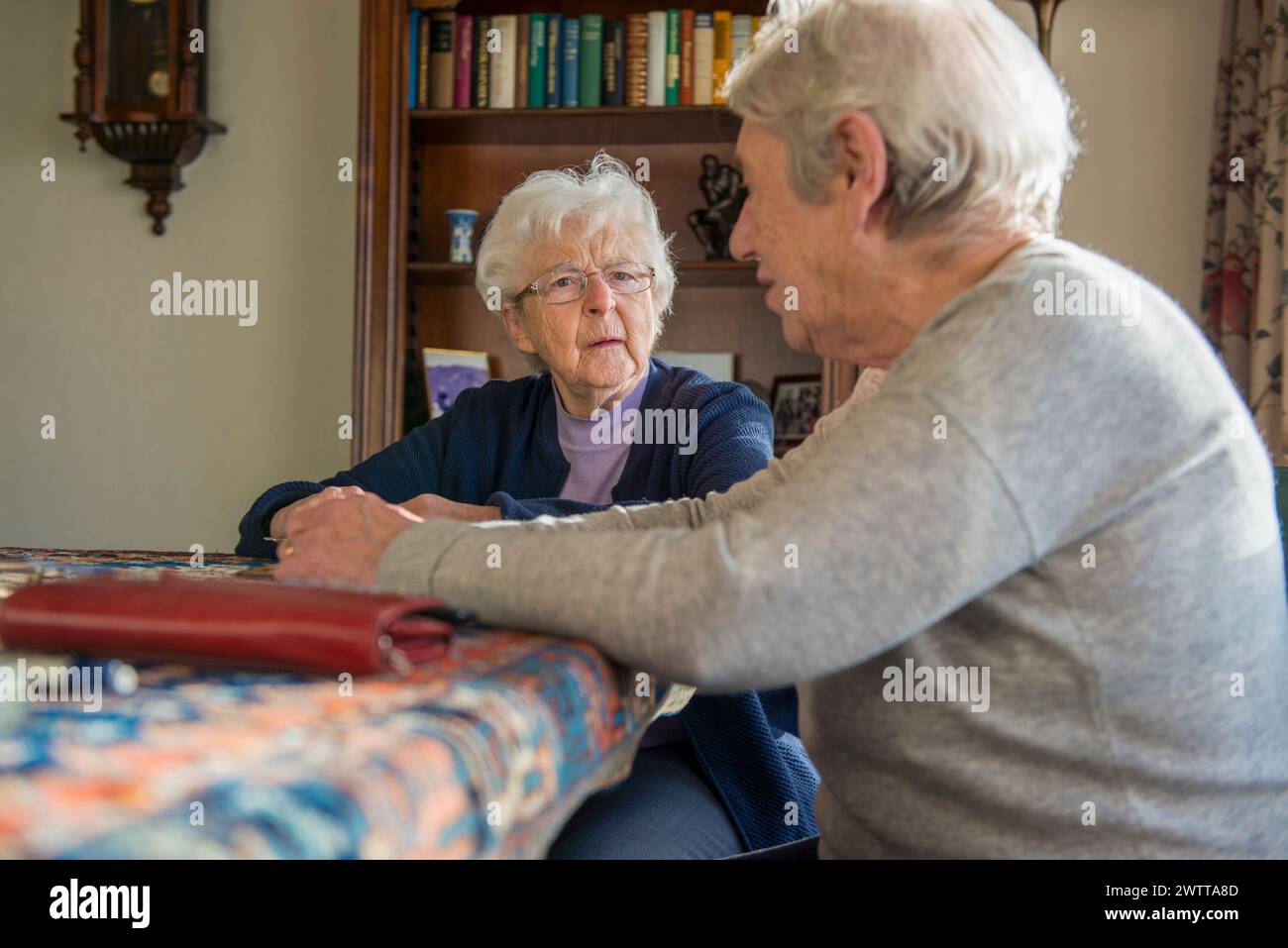 Due donne anziane condividono un momento di connessione con un album fotografico in un ambiente accogliente. Foto Stock