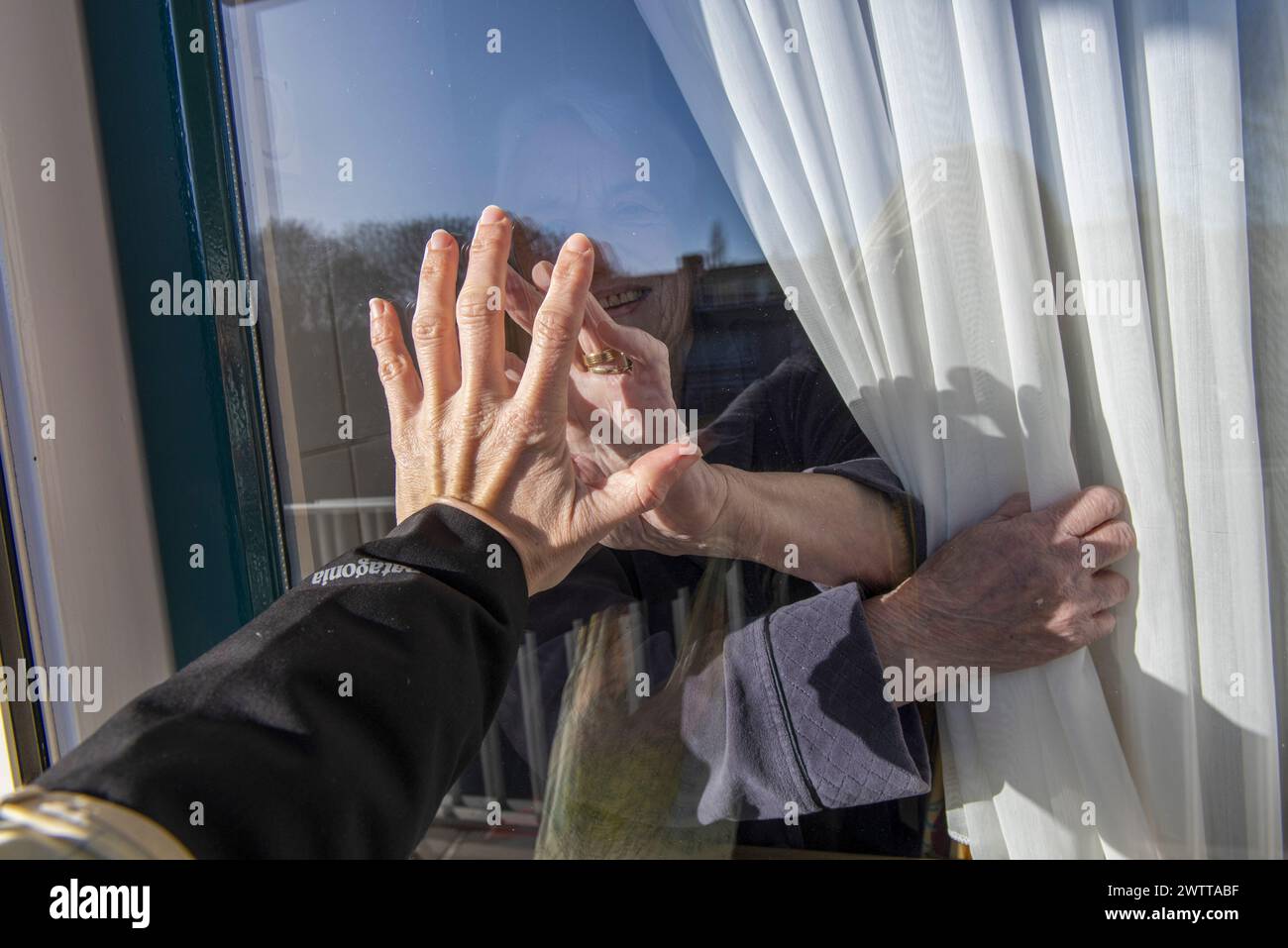 Due mani toccano attraverso una finestra di vetro, collegandosi ma separati Foto Stock